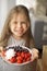 A little girl is holding a plate with breakfast berries, sunlight from the window and a happy baby