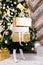 Little girl holding stack of wrapped presents standing beside decorated christmas tree at home