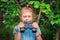 A little girl holds binoculars in her hands. A serious child observes the situation. The baby hid in greenery and is sitting in