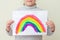 Little girl holds drawn rainbow on sheet of paper