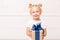 A little girl holds a gift box wrapped in blue ribbon in her outstretched hands. Selective focus