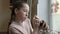 A little girl holds a huge pet snail in her hands, smiles and looks at it, standing at the window in her room. Close-up