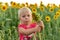 A little girl holds a small sunflower by the stalk, among the field of sunflowers