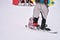 A little girl holds on to her mom`s leg while sitting on her snowboard. The woman climbs up the slope, holding on to the crossbar