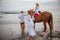 Little girl on a horse. Father leading horse by its reins on the beach. Horse riding by the sea. Mother walking near by. Family