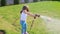 Little girl with a hose in her hands watering a green lawn