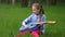 Little girl in a jeans jacket having fun and play guitar at springtime sitting in green grass against forest