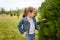 Little girl in jeans jacket posing outdoors in spring park touching green bush leaves. Interested clever child, exploring