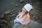 Little girl in jeans and a pink vest sits on a stone by the sea and smiles