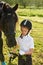 Little girl jockey communicating with her black horse in professional outfit