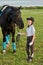 Little girl jockey communicating with her black horse in professional outfit