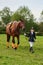 Little girl jockey lead horse by its reins across country in professional outfit
