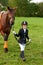 Little girl jockey lead horse by its reins across country in professional outfit