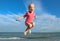 Little girl jumping and hovering in the air on the background of blue sky and summer sea. Happy child girl playing at beach and