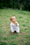 Little girl kneels on a green meadow with an apple in her hand