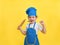 a little girl is laughing in a kitchen apron and hat with a rolling pin in her hand on a yellow background. A cute girl in a blue