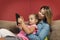 Little girl laying on couch with her mother using tablet