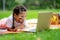 Little girl laying down with tablet sitting in the park. Curious kid searching with magnifying on the grass in the park