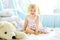 Little girl in light bedroom with big white teddy bear