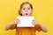 A little girl with light hair on a yellow background. Isolated. A child in a yellow dress makes notes on a book. Mockup.