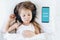 Little girl listening to children`s audiobook in mobile phone in headphones before sleeping in bed. Education, child development.