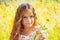 Little girl with long hair in a white dress rejoices in a field with flowers