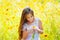 Little girl with long hair in a white dress rejoices in a field with flowers