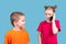 Little girl looking at her smiling little brother, talking on a smartphone, isolated on blue background