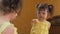 A little girl is looking in the mirror. A beautiful girl with tails on her head leans in front of the mirror. A child in a yellow