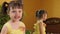 A little girl is looking in the mirror. A beautiful girl with tails on her head leans in front of the mirror. A child in a yellow