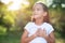 Little girl looking up to at sky with hands on chest, summer nature outdoor. Happy smiling kid feels grateful, wishes dream come