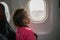 A little girl looks out the window of the plane. Portrait of a child in the seat of a passenger airliner. The child is traveling