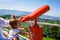 A little girl looks through red binoculars on a viewing platform with a panorama of the city.