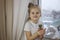 A little girl lovingly holds in her hands a cactus sitting on the windowsill