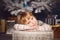 Little girl lying on big present near the christmas tree