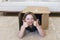 Little girl lying down in brown cardboard box making a double thumbs up sign
