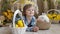 Little girl is lying on the floor next to a white rabbit and Easter eggs of different colors.