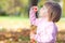 Little girl making bubble blower on the autumn forest