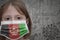 Little girl in medical mask with flag of afghanistan stands near the old vintage wall with text coronavirus, covid, and virus