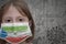 Little girl in medical mask with flag of equatorial guinea stands near the old vintage wall with text coronavirus, covid, and