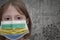 Little girl in medical mask with flag of gabon stands near the old vintage wall with text coronavirus, covid, and virus picture