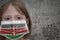 Little girl in medical mask with flag of kenya stands near the old vintage wall with text coronavirus, covid, and virus picture