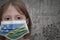 Little girl in medical mask with flag of Solomon Islands stands near the old vintage wall with text coronavirus, covid, and virus