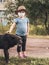 Little girl in a medical mask stroking a large homeless black dog outdoors