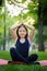 A little girl meditates in the park in the lotus position the girl does yoga raised her hands up and folded her palms