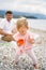 Little girl with a mold in her hand stands on a pebble beach against the background of a sitting dad