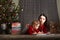 Little girl and mom in a red sweater with a deer for the New Year. A girl and a sister are reading a book by the Christmas tree at