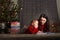 Little girl and mom in a red sweater with a deer for the New Year. A girl and a sister are reading a book by the Christmas tree at