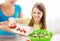 Little girl with mother adding tomatoes to salad
