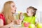 Little girl and mother with baby food feeding each other, sitting at table in nursery